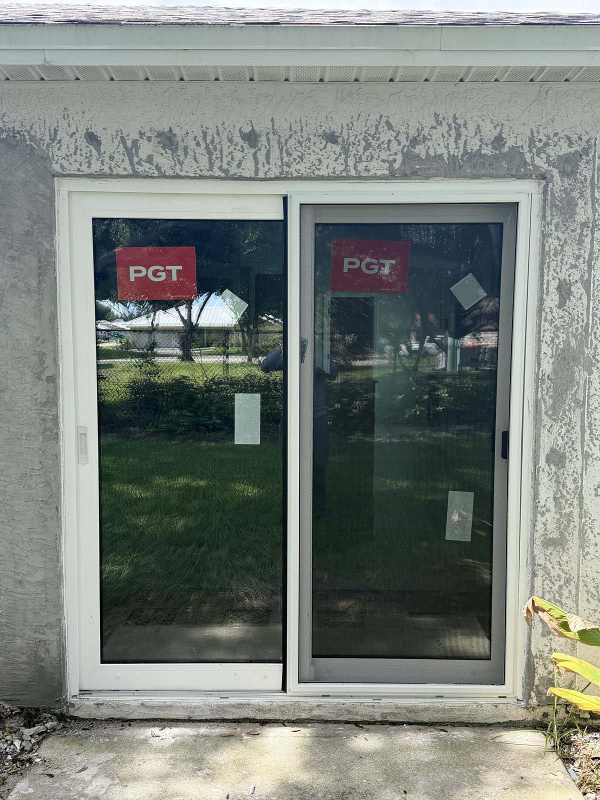 New sliding glass door installed in a stucco opening with manufacturer labels still on the glass