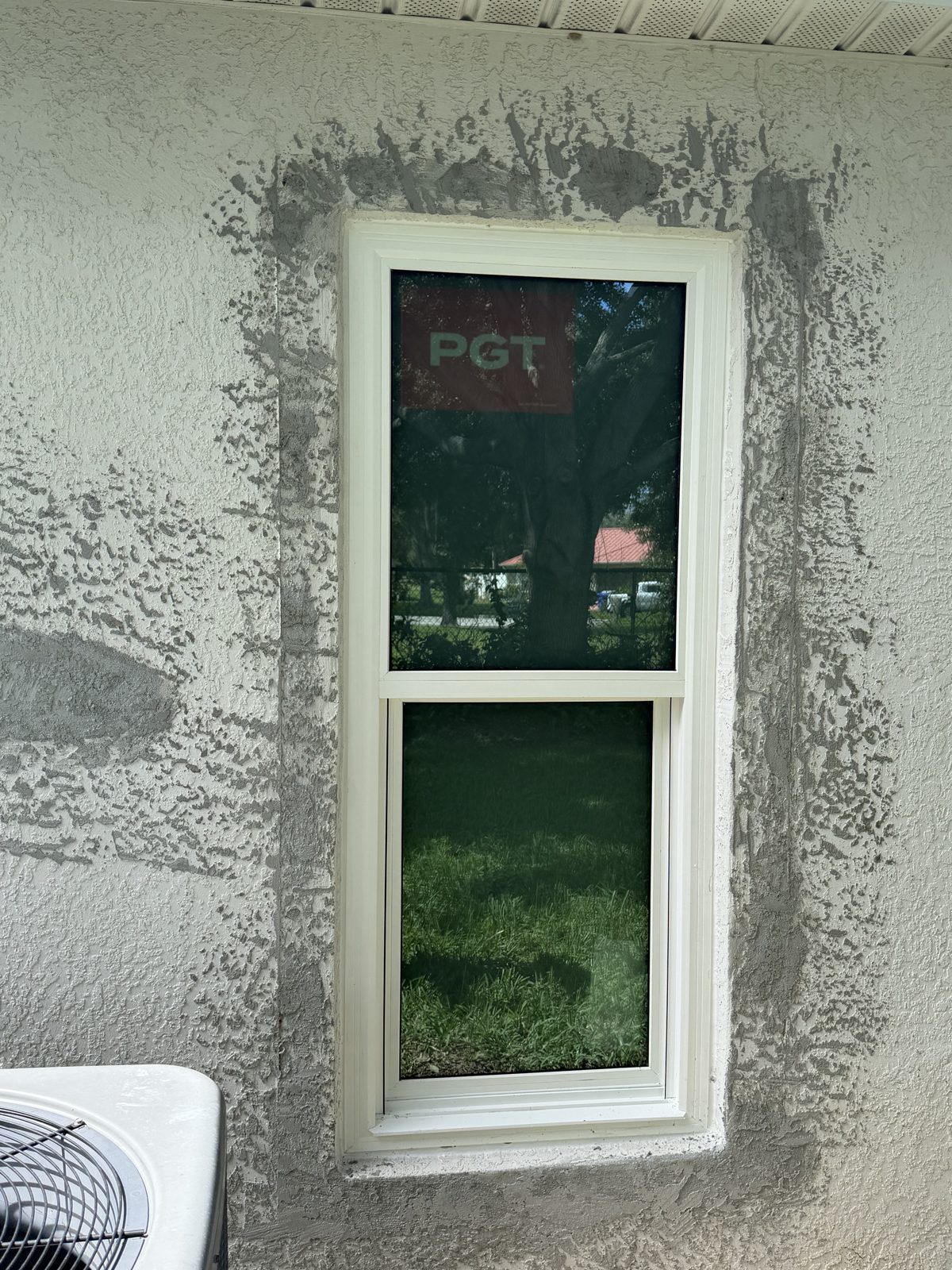 White replacement window installed in an exterior stucco wall with the manufacturer label still on the glass