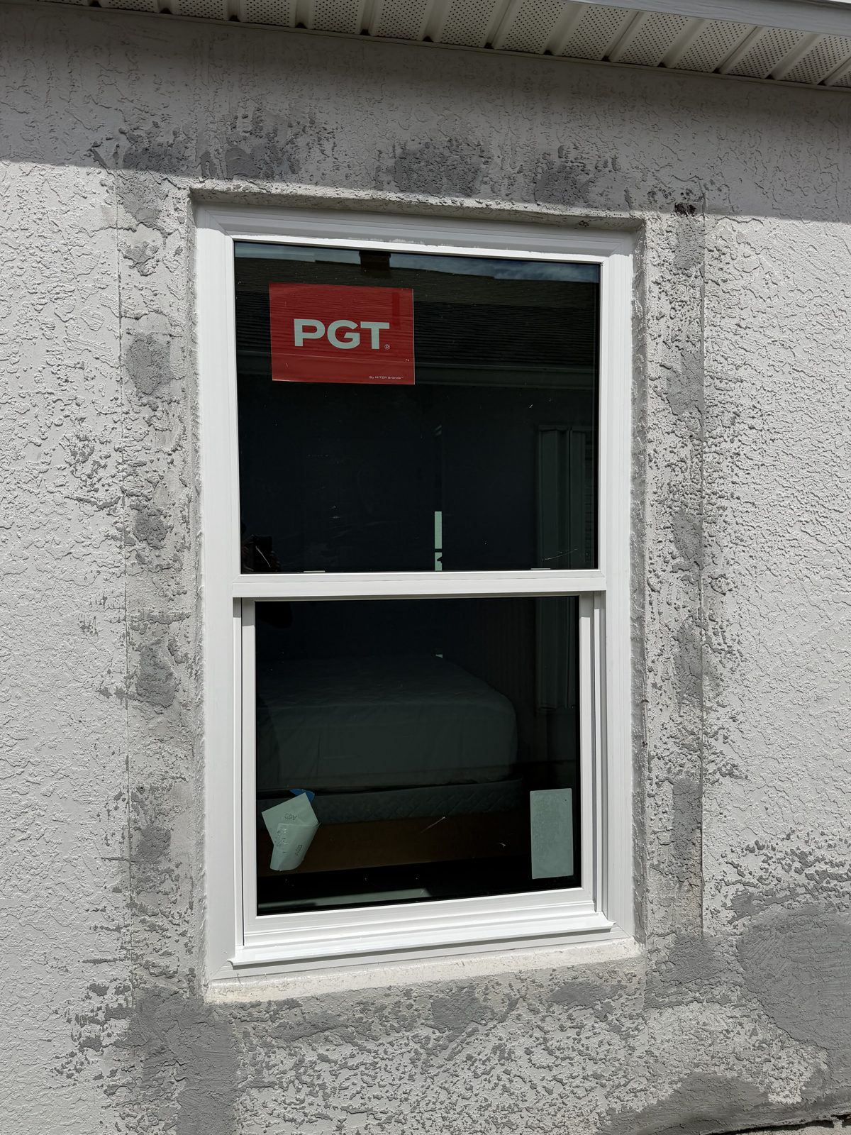 Cream-framed replacement window with a fresh stucco border beside an air conditioning unit